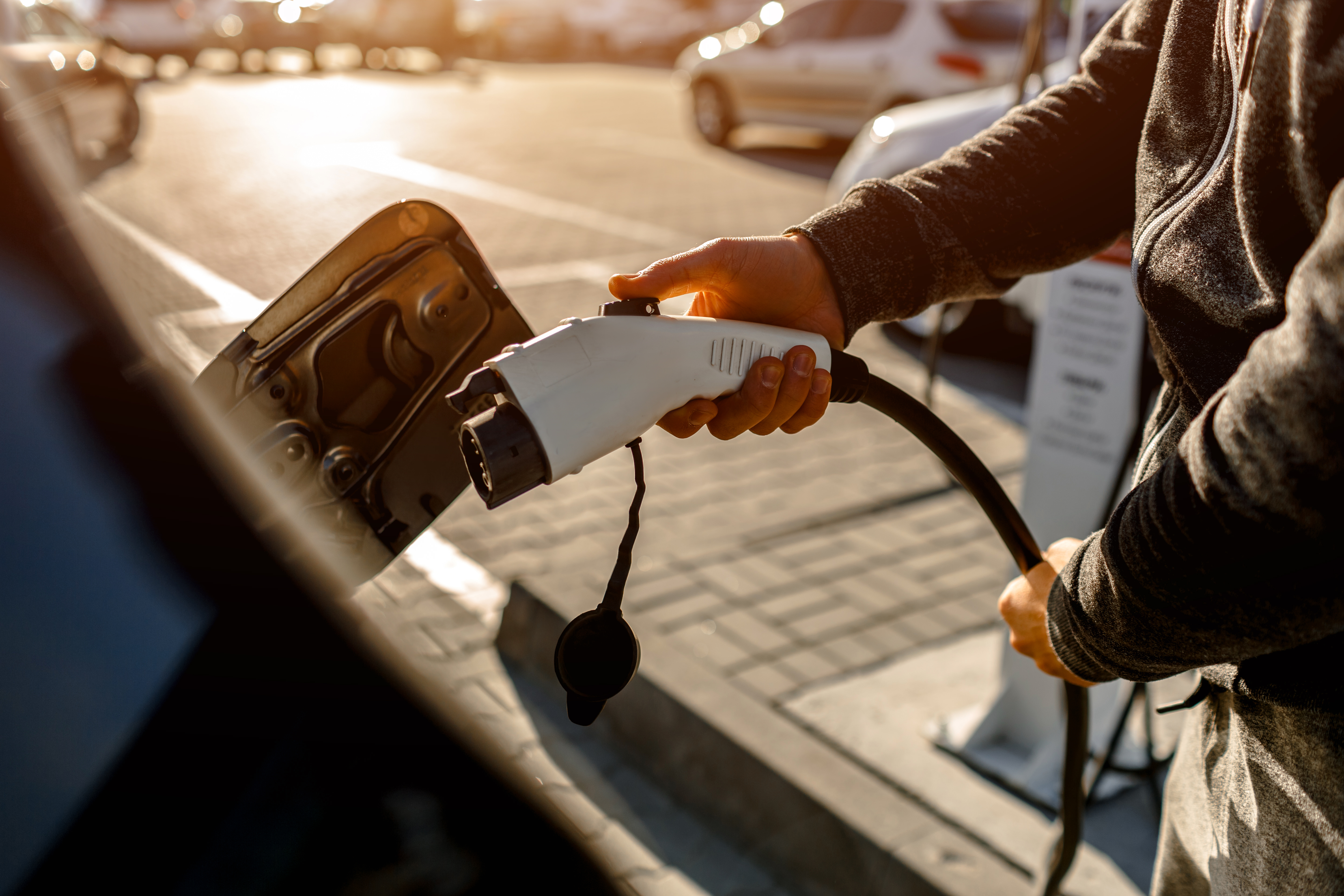 man holding power charging cable for electric car in outdoor car park